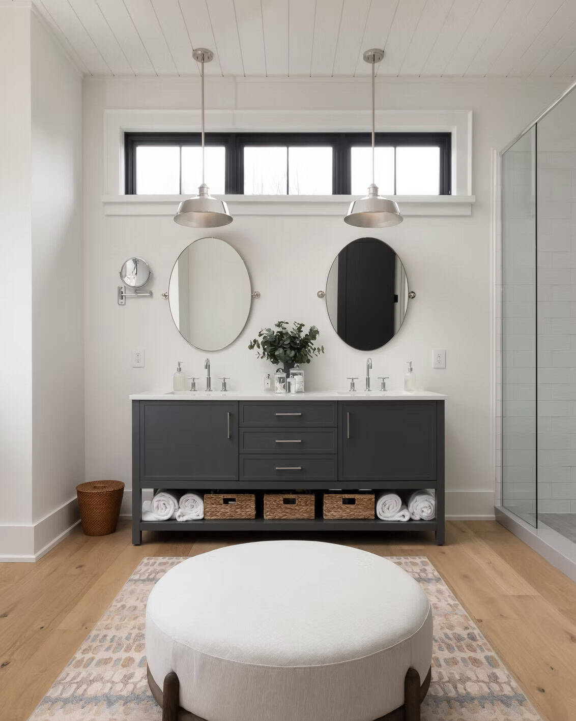 Primary bathroom double vanity with dark cabinetry, dual oval mirrors, silver pendants, and woven basket storage
