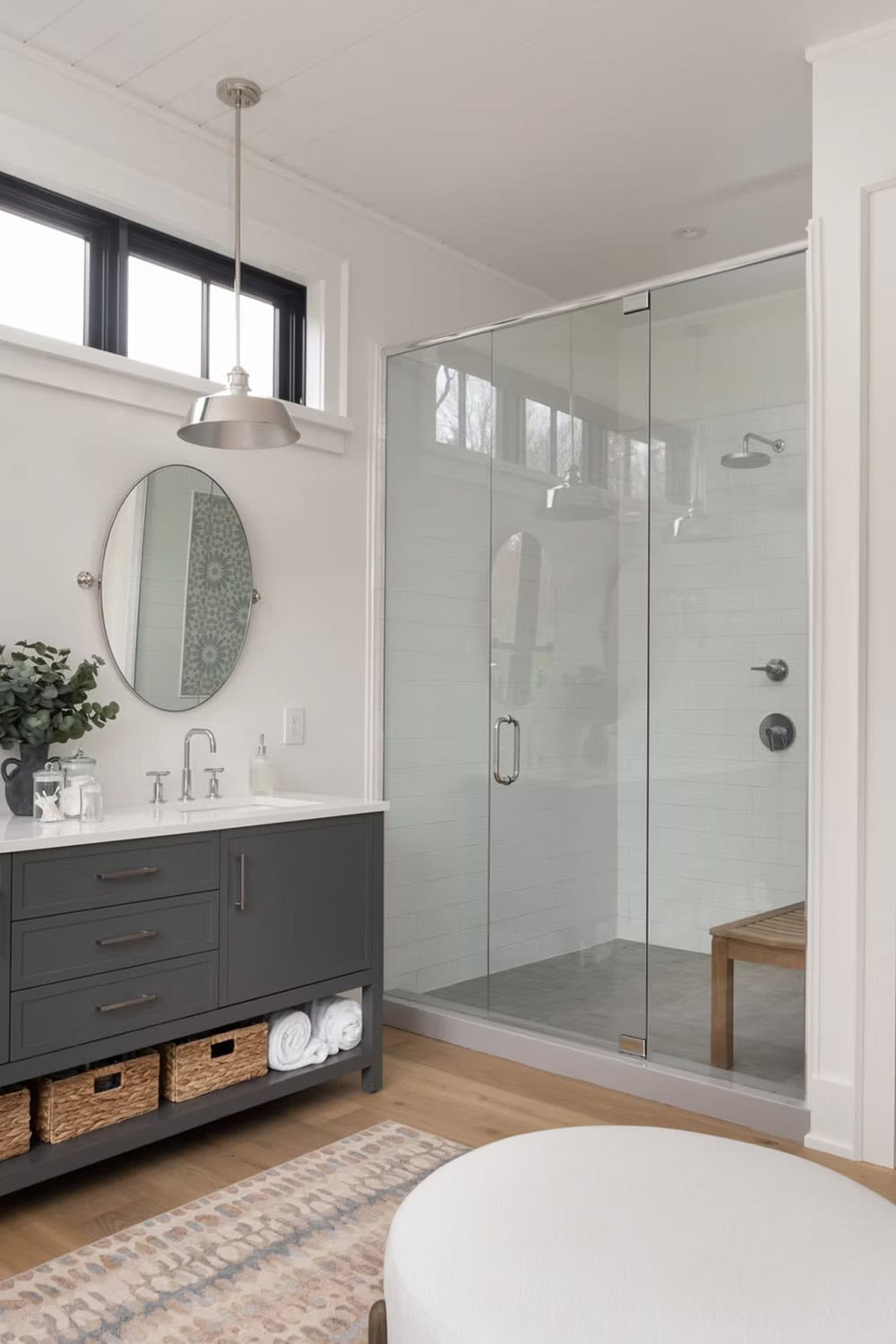 Primary bathroom with dark vanity, round mirror, glass-enclosed shower, and silver pendant light