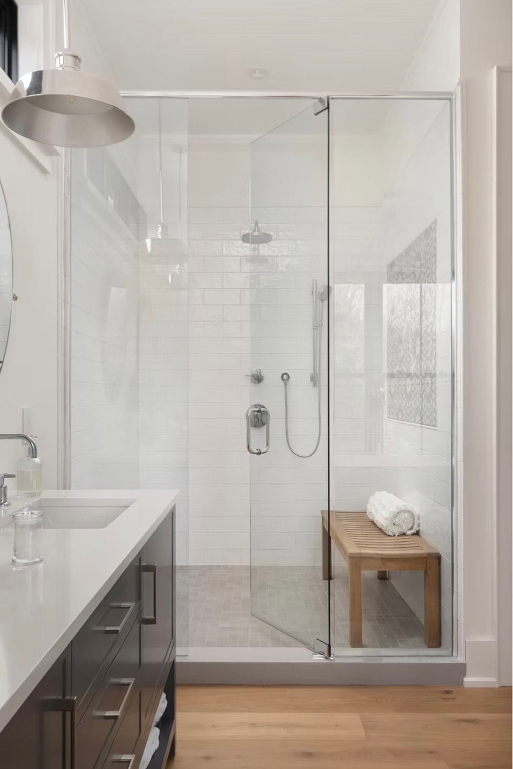 Glass-enclosed walk-in shower with white subway tile, rain showerhead, and teak bench