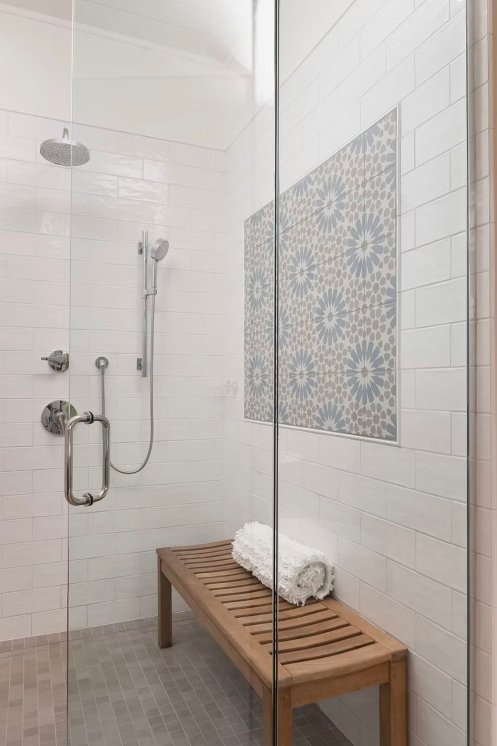 Walk-in shower interior with white subway tile, patterned accent tile niche, rain showerhead, and teak bench