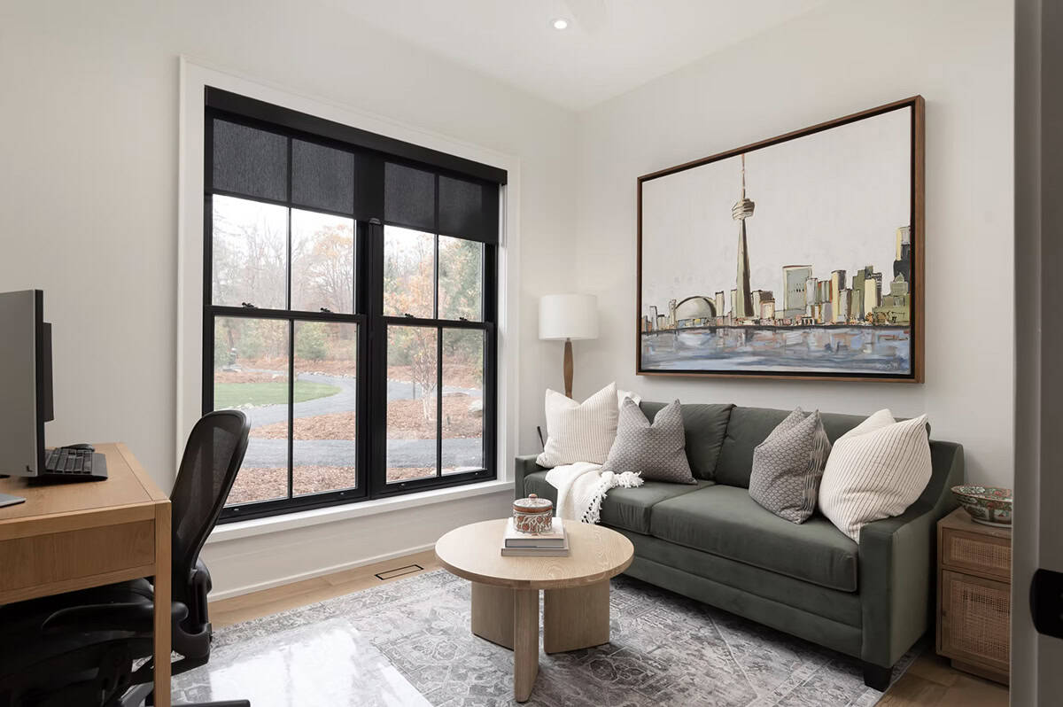 Home office and sitting room with green sofa, Toronto skyline painting, black-framed windows, and wood desk