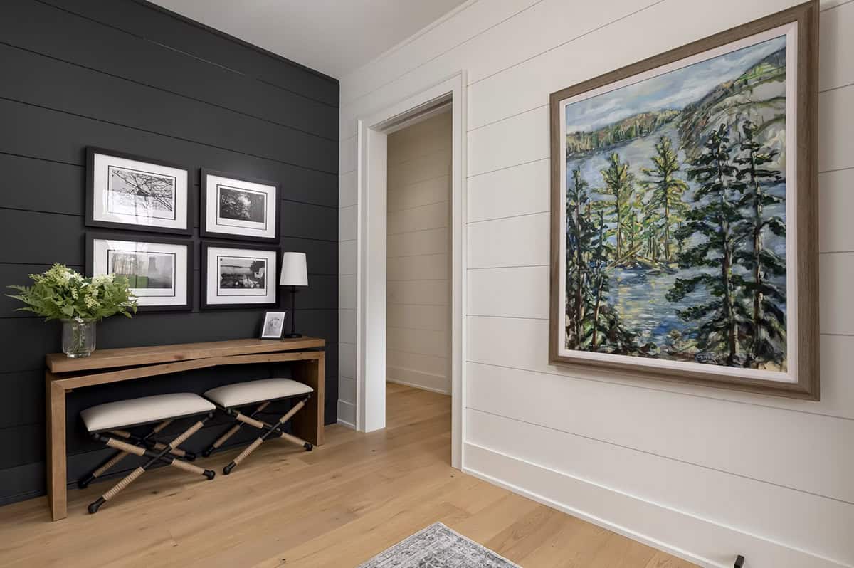 Cottage foyer with dark shiplap accent wall, black-and-white photo gallery, console table, and landscape painting