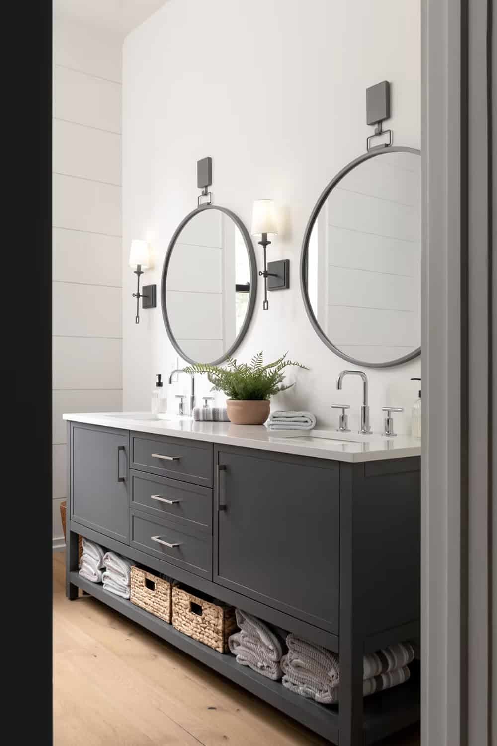 Guest bathroom double vanity with dual round mirrors, dark cabinetry, chrome sconces, and woven basket storage