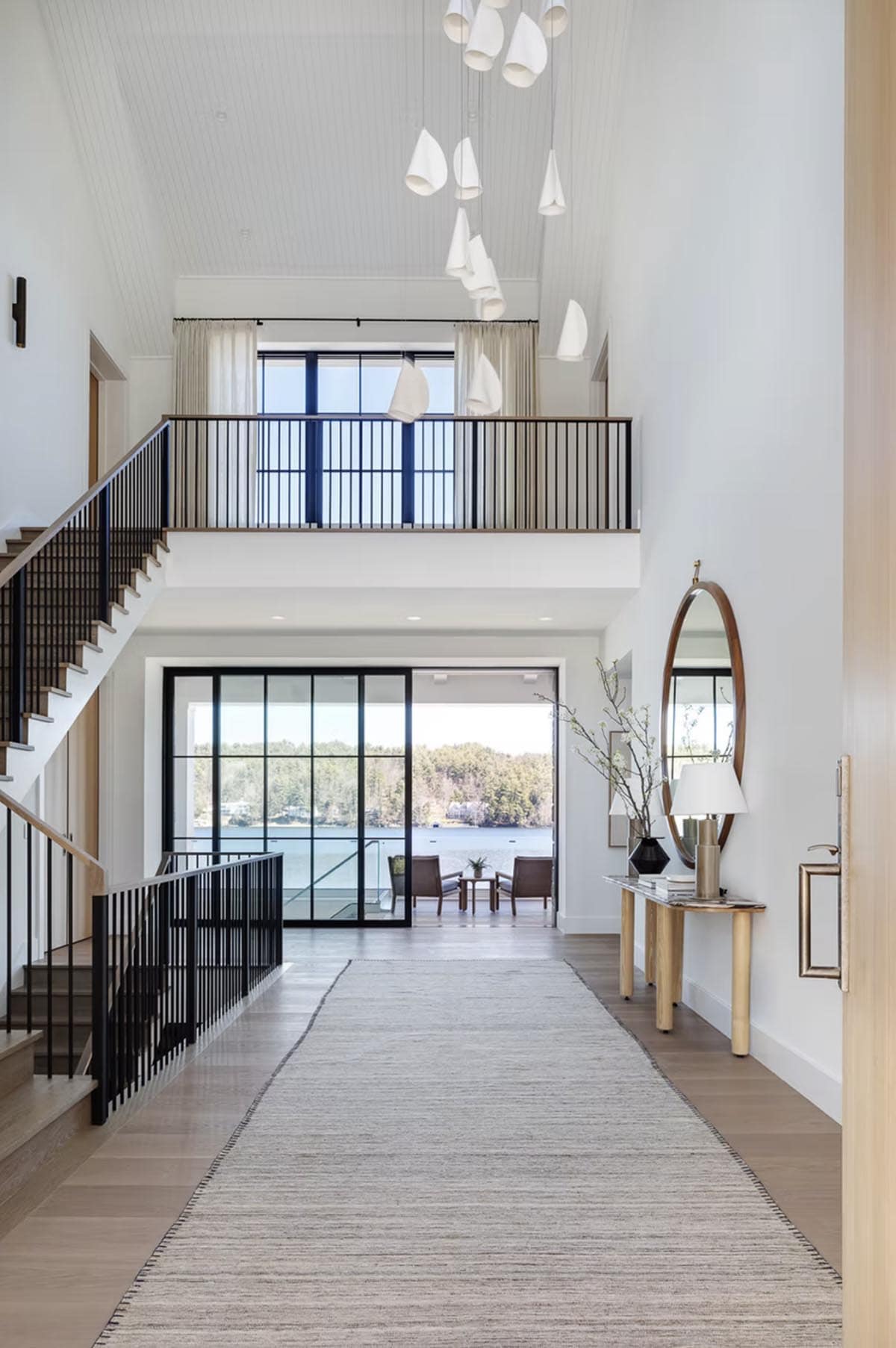 Grand hallway with soaring ceilings, cascading white pendant lights, and floor-to-ceiling lake views through steel-framed glass doors