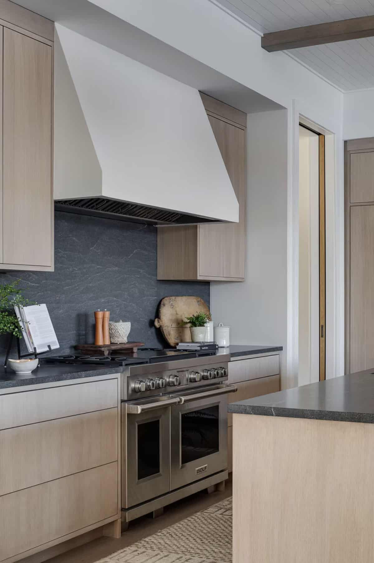 Wolf range with white plaster hood, dark stone backsplash, and light oak cabinetry in luxury kitchen