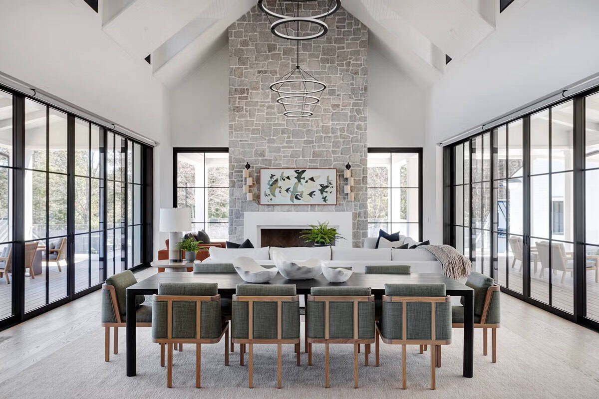 Cathedral-ceiling great room with stone fireplace, dining table for ten, black steel doors opening to outdoor terraces
