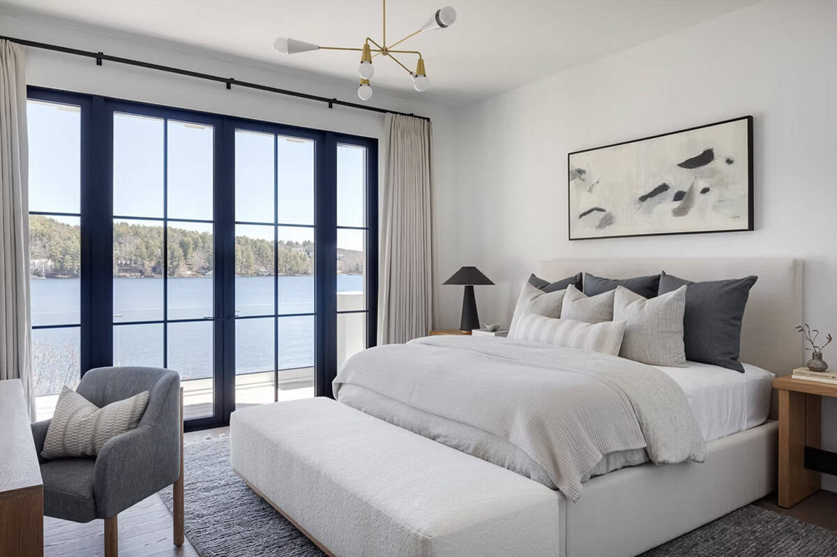 Serene bedroom with lake views through black-framed French doors, upholstered bed, and mid-century brass chandelier