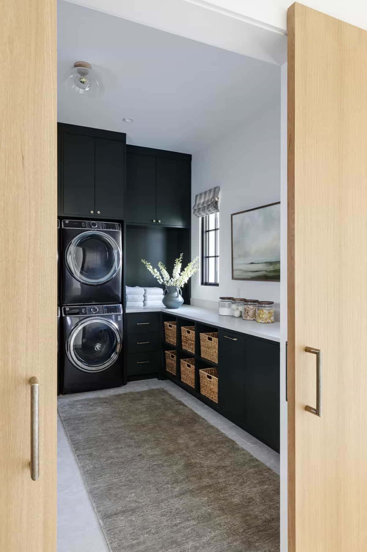 Laundry room with deep forest green cabinetry, stacked washer-dryer, woven storage baskets, and white countertops