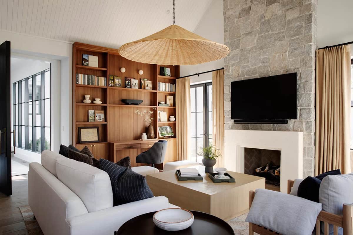 Cozy sitting room with walnut built-in bookcase, oversized rattan pendant, stone fireplace with wall-mounted TV, and white linen sofa