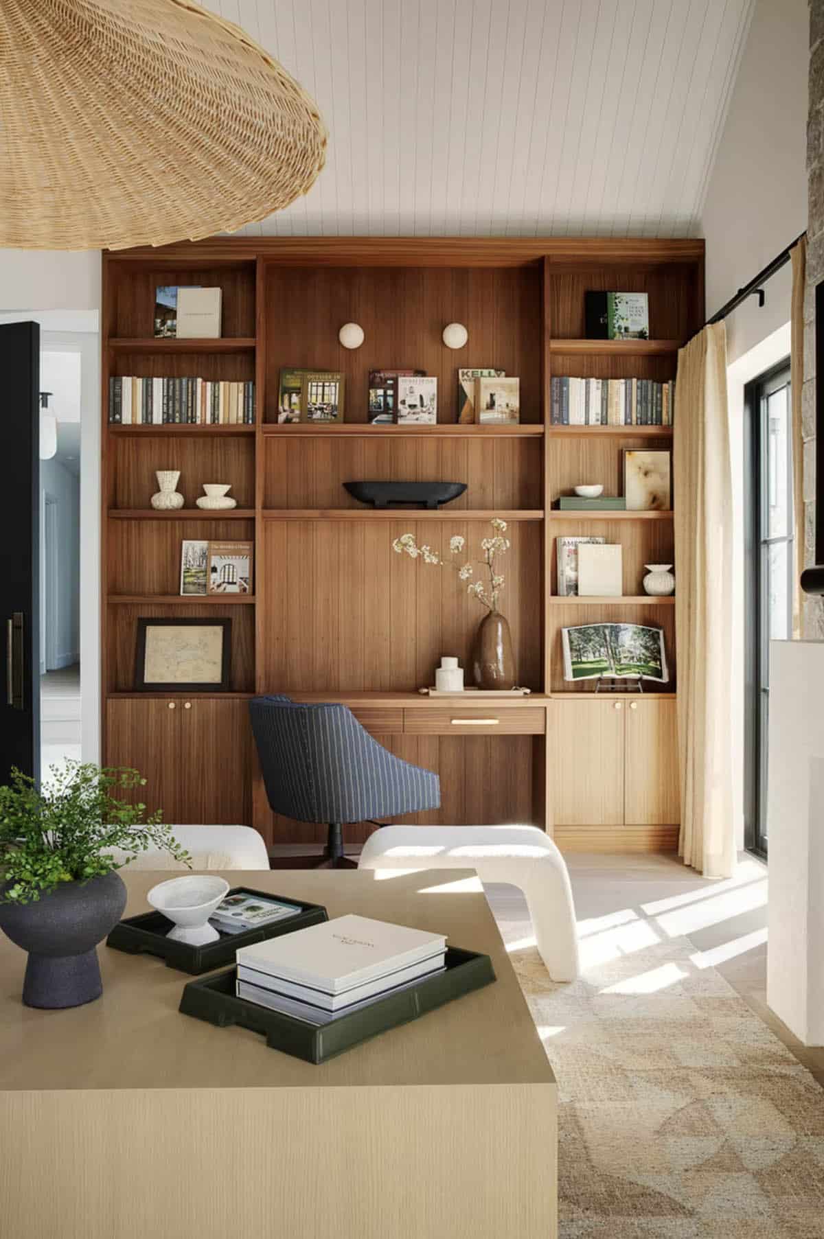 Close-up of walnut built-in shelving unit with integrated desk, striped office chair, and decorative books and ceramics