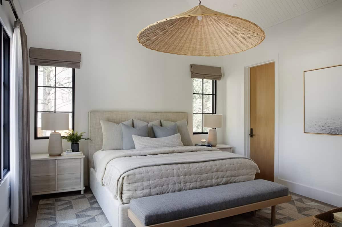 Guest bedroom with oversized rattan pendant light, linen upholstered bed, geometric patterned rug, and black-framed windows