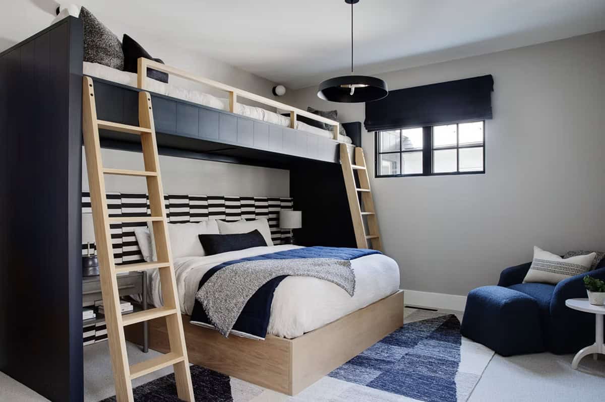 Kids' bunk room with navy built-in loft bed, natural wood ladders, striped headboard wall, and blue upholstered lounge chair