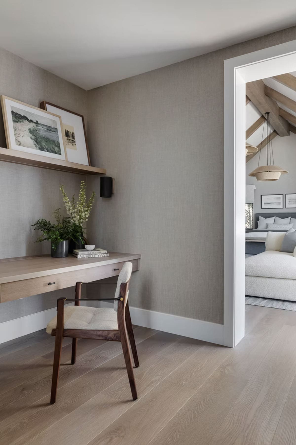 Home office alcove with floating oak desk, picture ledge shelf, textured wallcovering, and view into vaulted primary suite