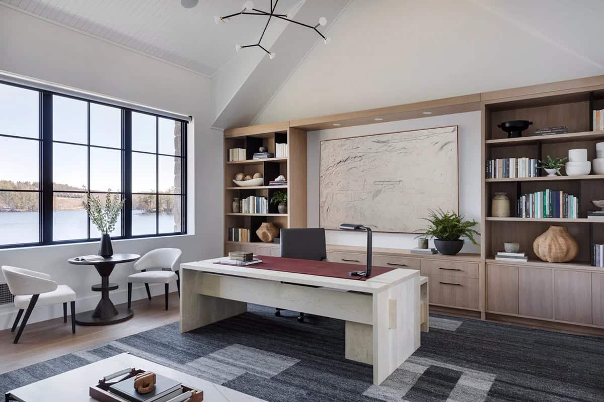 Lake-view home office with light oak desk, floor-to-ceiling built-ins, abstract artwork, and sculptural branch chandelier