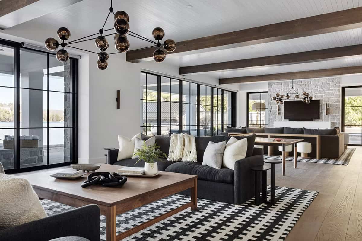 Lower-level recreation room with dark sectional sofas, globe chandelier, ping pong table, stone fireplace, and black steel doors