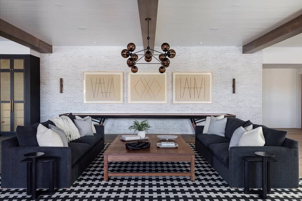 Lower-level lounge with dual dark sofas, geometric triptych artwork, white brick accent wall, and bronze globe pendant