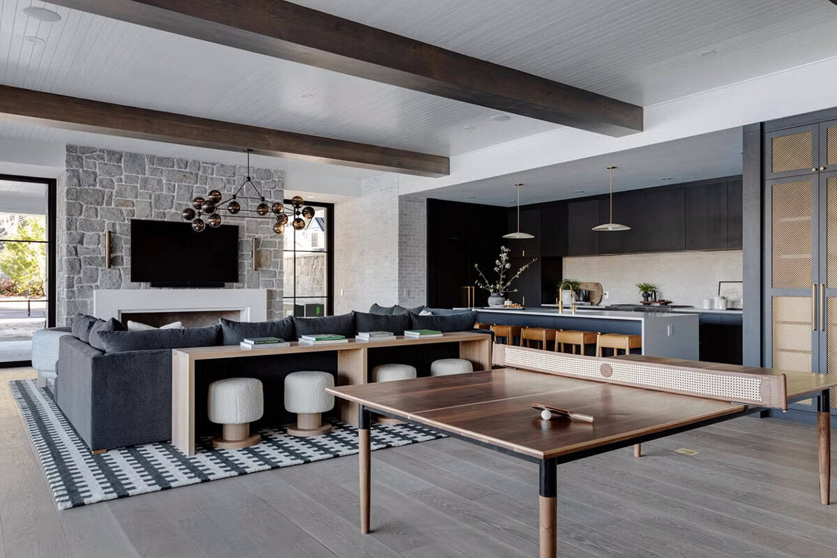 Open-plan lower level with ping pong table, dark sectional, stone fireplace, and dark cabinetry kitchen beyond