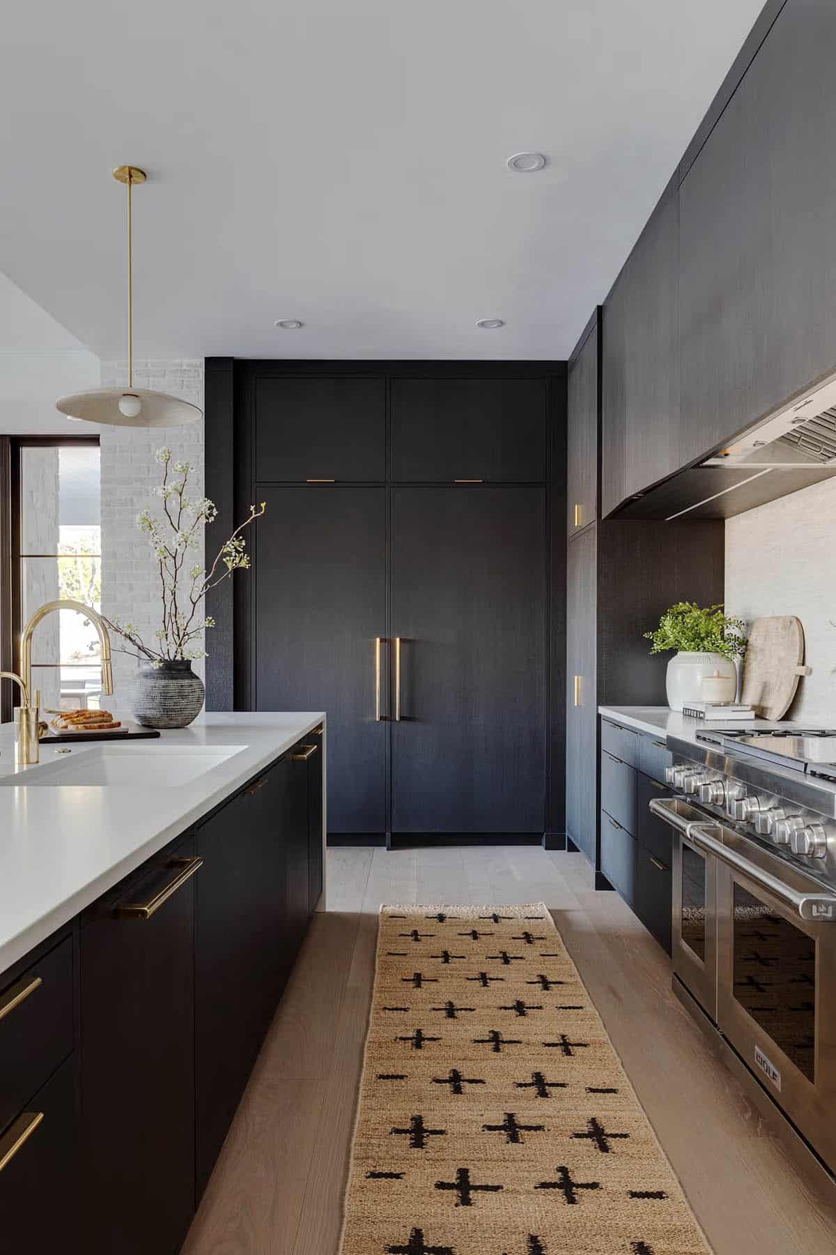 Dark lower-level kitchen with charcoal cabinetry, brass hardware, Wolf range, white quartz island, and jute runner