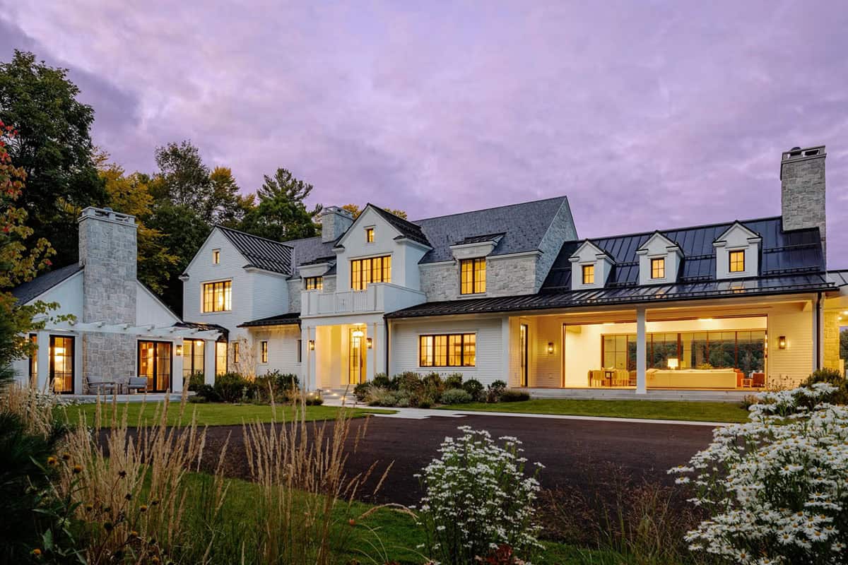 Twilight exterior of luxury New Hampshire lake house with glowing interiors, white clapboard and stone facade