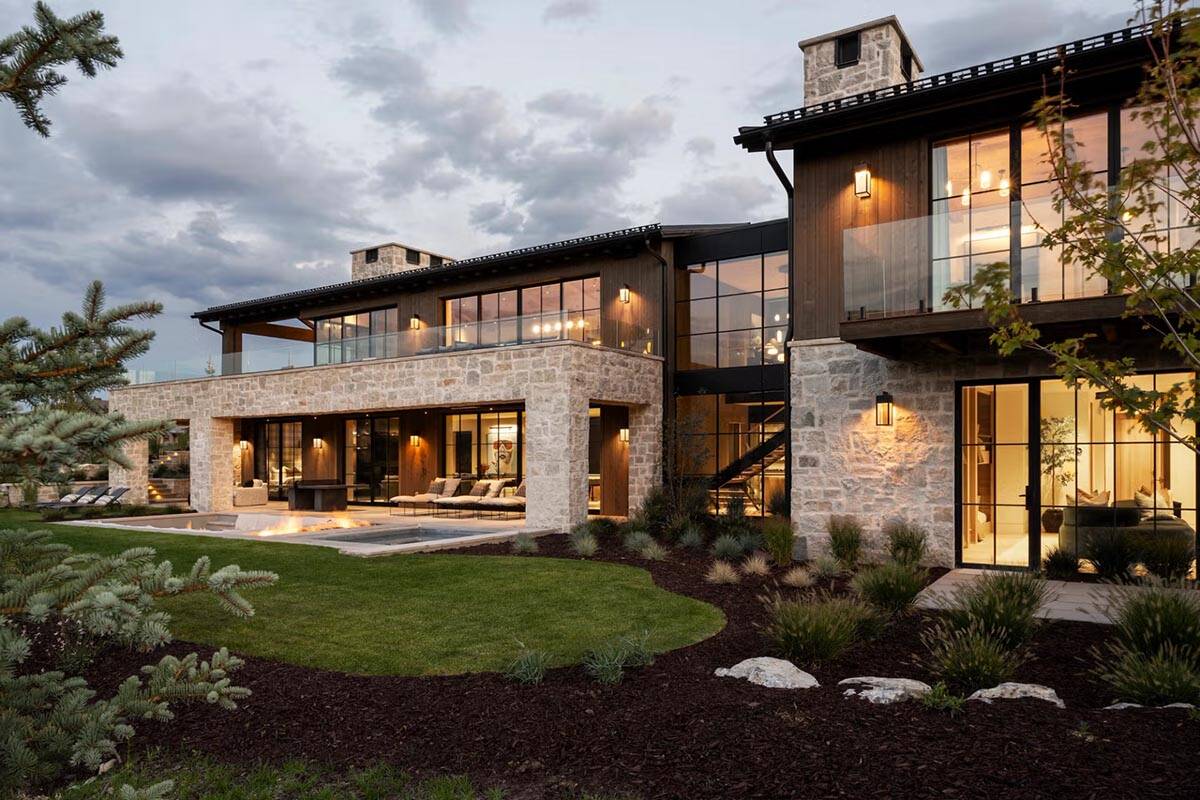 Luxury modern mountain home exterior at dusk with stone facade, wood siding, and illuminated interiors