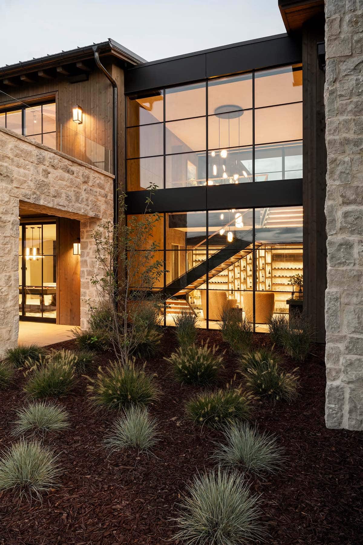 Two-story glass curtain wall revealing staircase and wine display inside mountain home