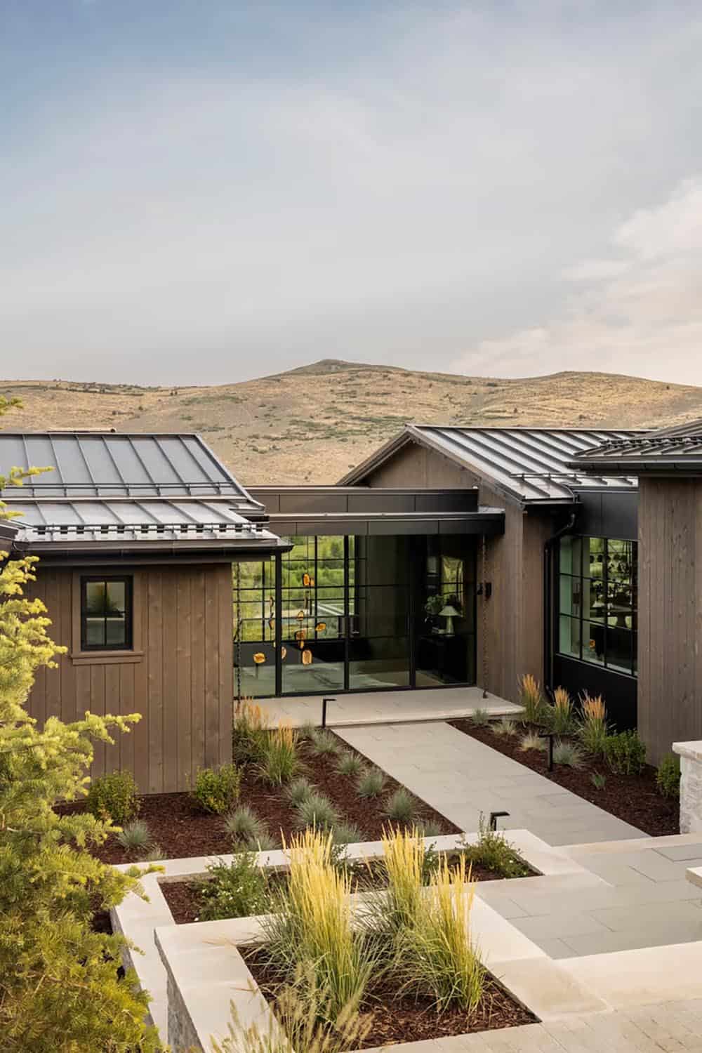 Modern mountain home entry with metal roof, steel-frame windows, and mountain backdrop