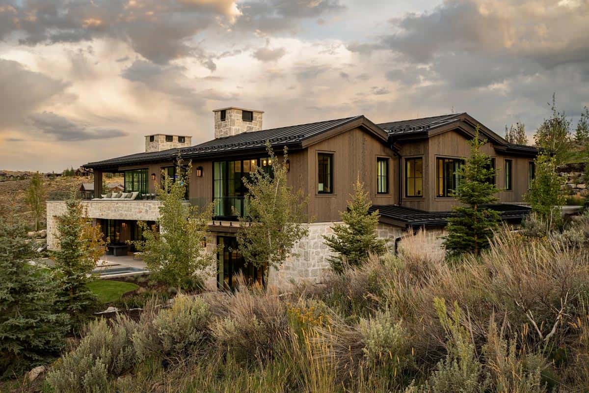 Contemporary mountain home exterior with stone chimney and sagebrush landscape at sunset