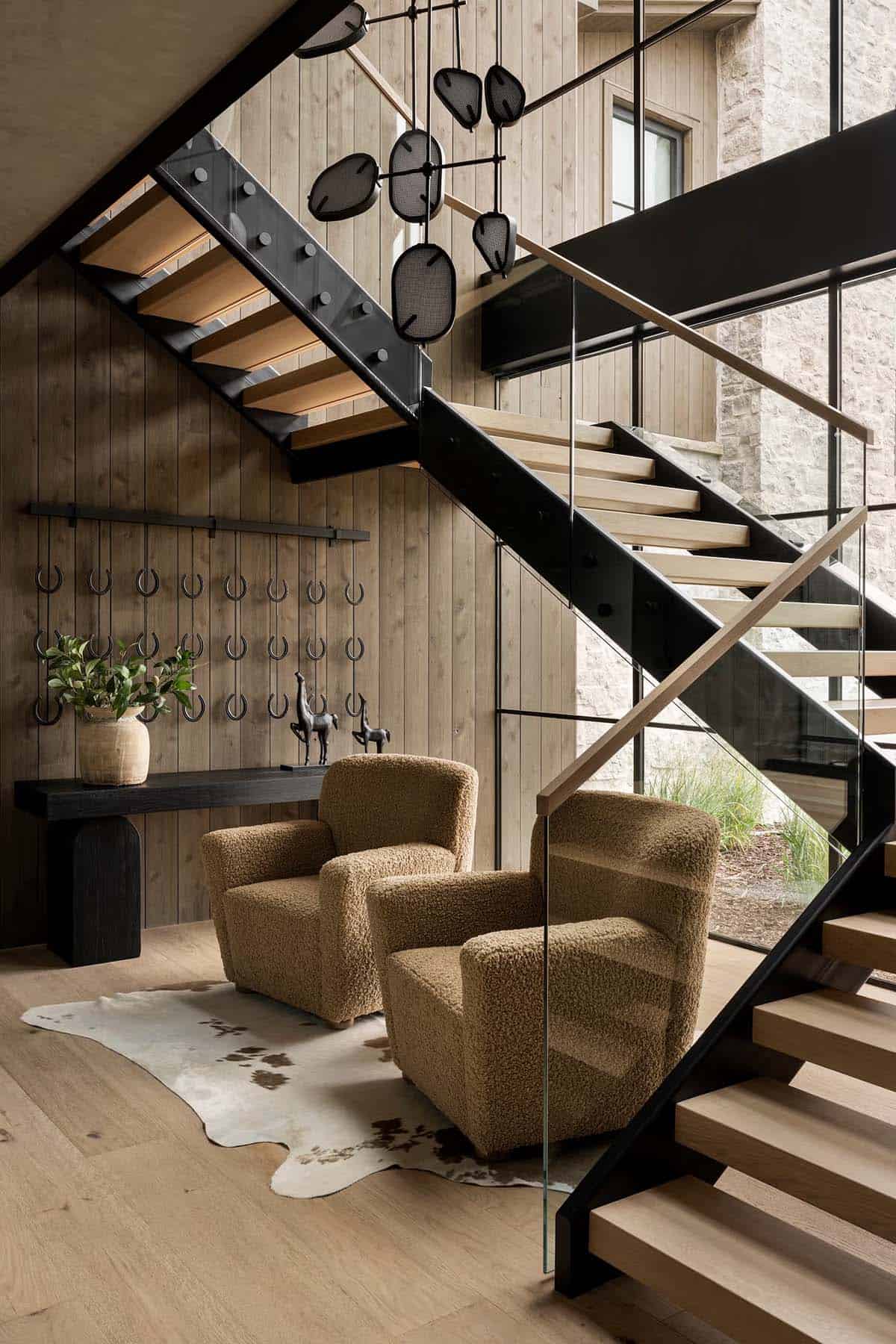Floating steel staircase with wood treads, glass railing, and boucle armchairs in entryway