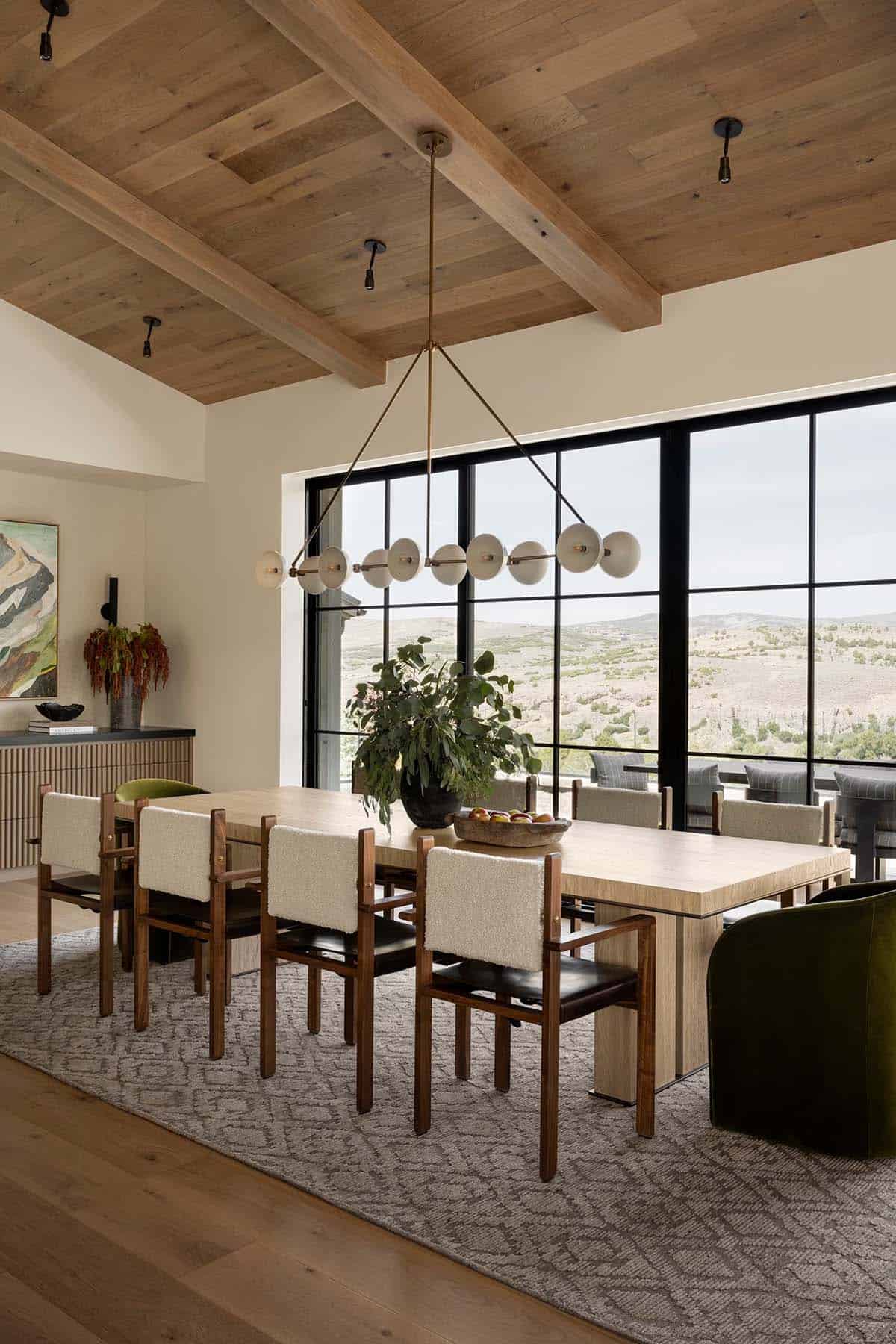 Dining room with wood beam ceiling, modern chandelier, and floor-to-ceiling mountain views