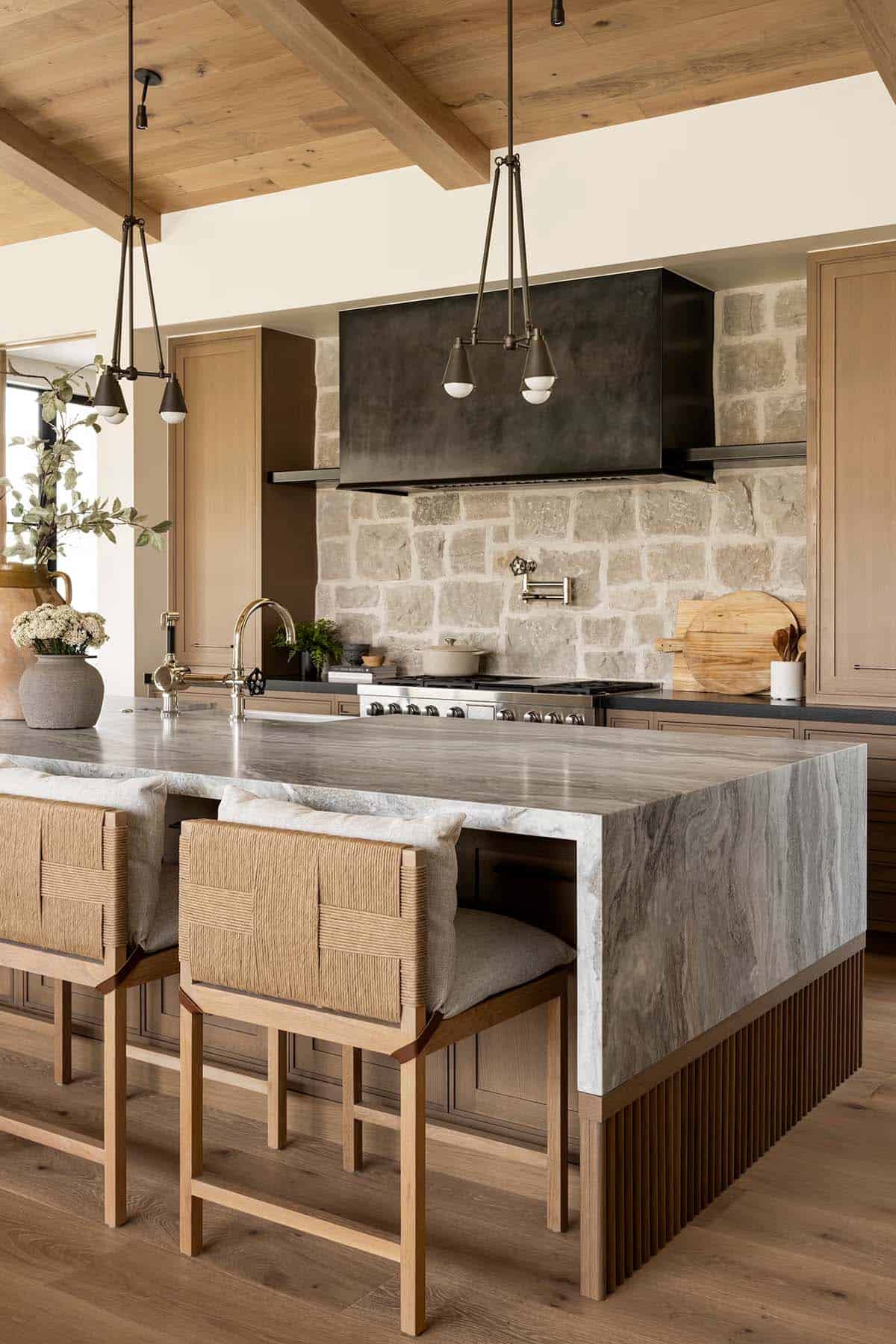 Kitchen island with marble waterfall countertop, stone backsplash, and black range hood