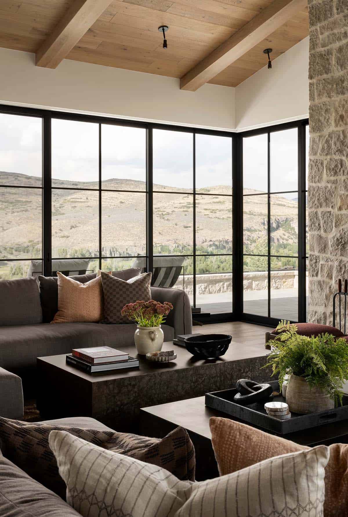 Living room corner with wraparound black-frame windows overlooking rugged mountain terrain