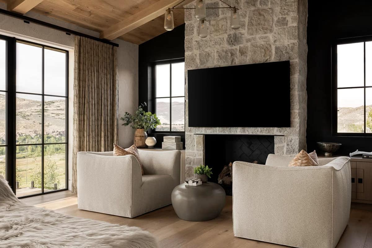 Primary bedroom sitting area with stone fireplace, cream boucle chairs, and mountain views