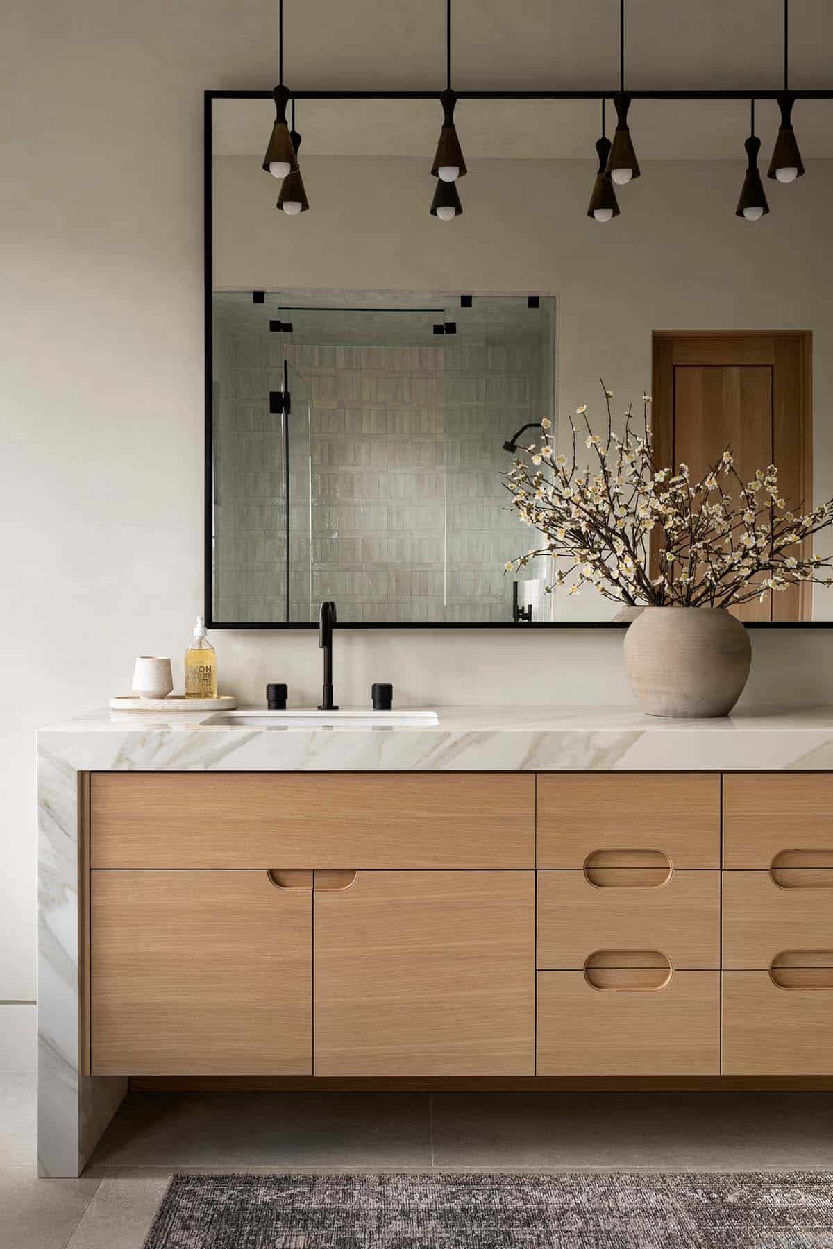 Bathroom vanity with light oak cabinetry, marble countertop, and black-frame mirror