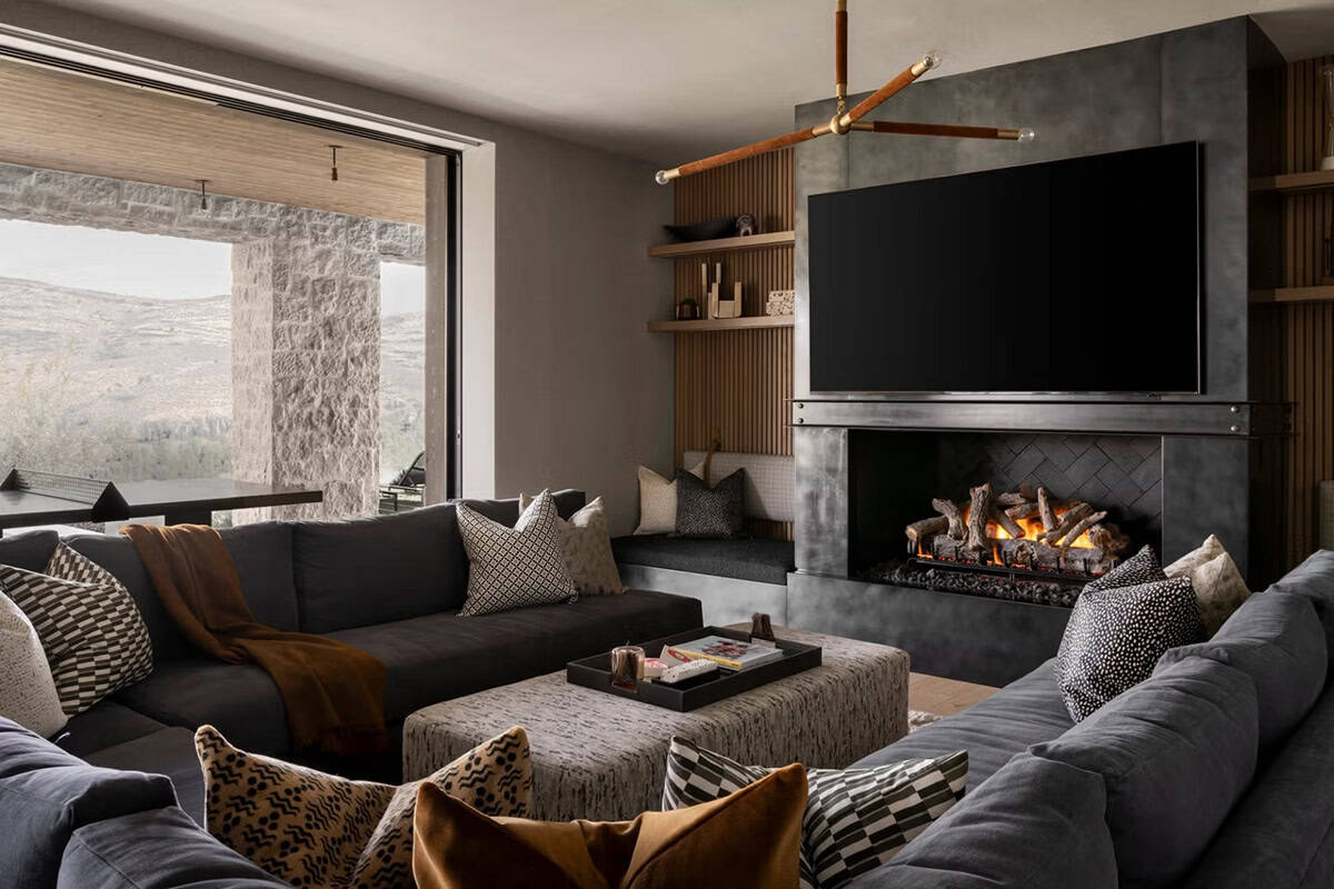 Lower-level lounge with dark sectional sofas, steel fireplace, and mountain views