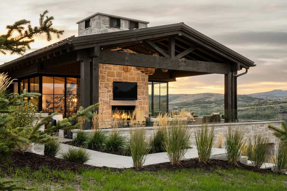 Covered outdoor living pavilion with stone fireplace, TV, and rolling hillside views at dusk