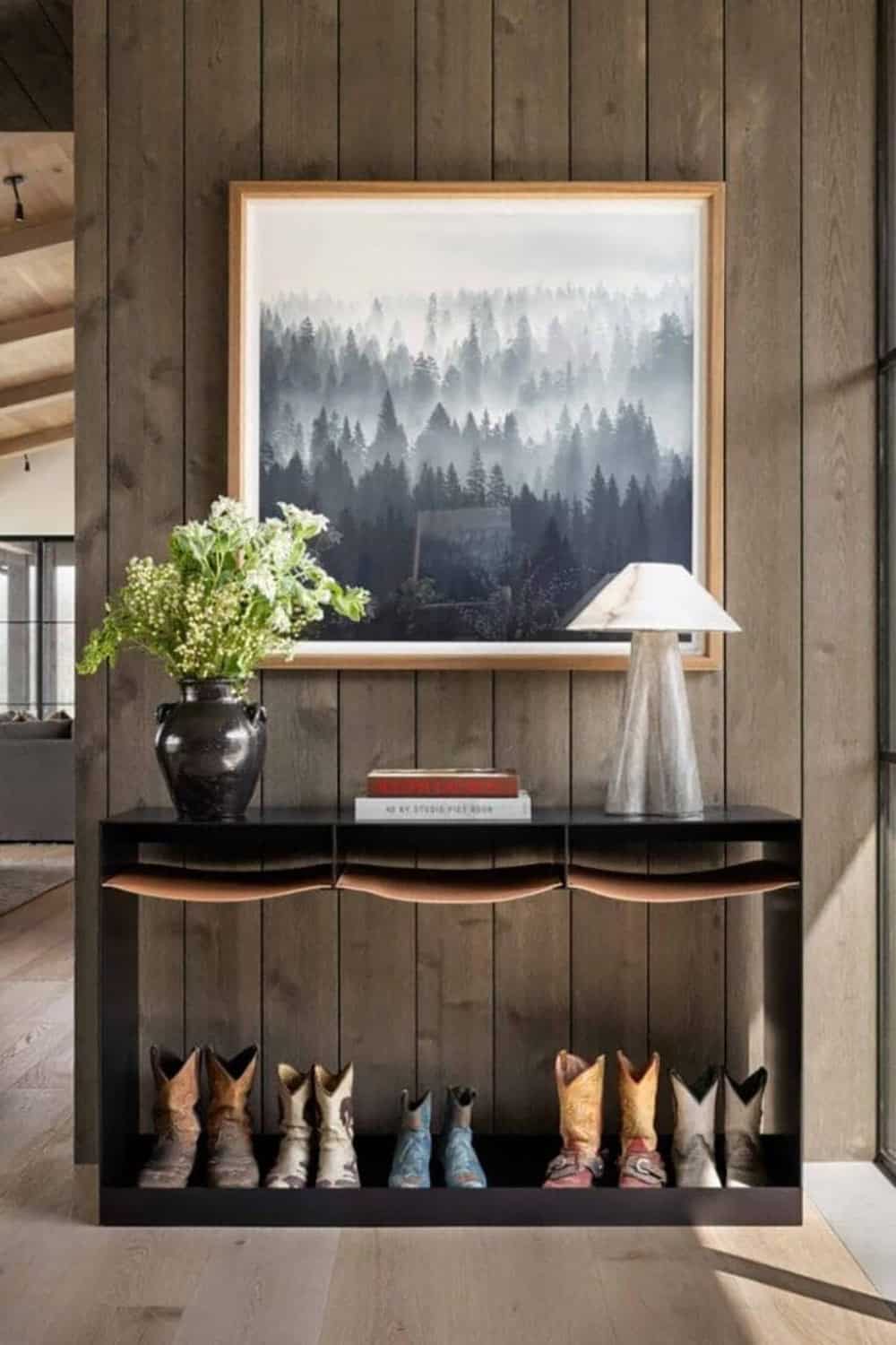 Entryway console with cowboy boots display shelf and misty forest landscape artwork