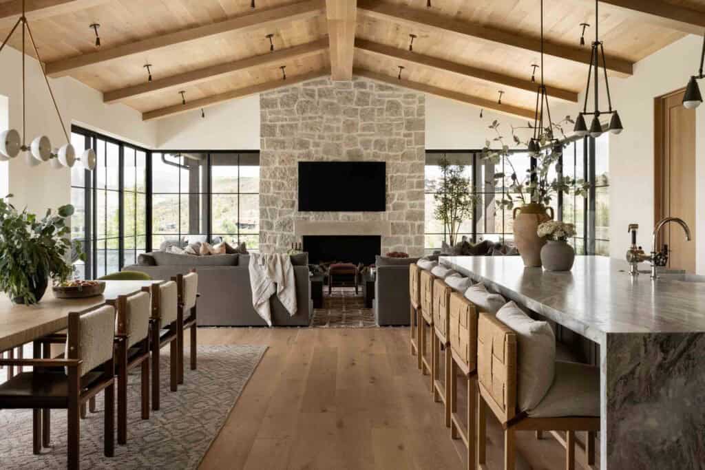 Wide-angle great room view showing kitchen island, dining, living area, and stone fireplace wall