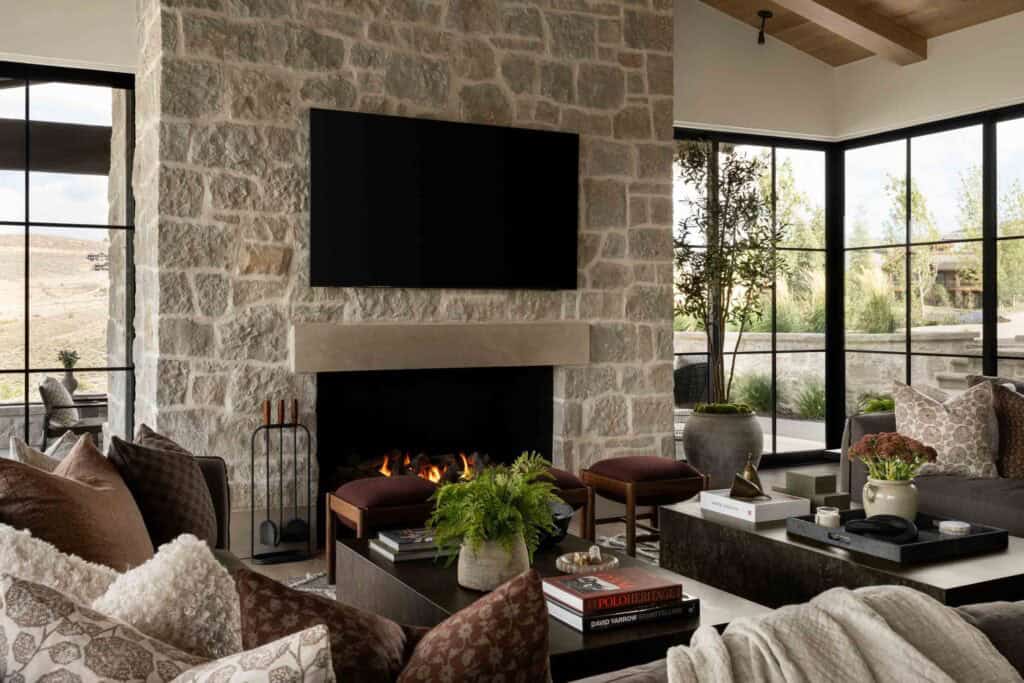 Living room stone fireplace with concrete mantel, TV, and flanking black-frame windows