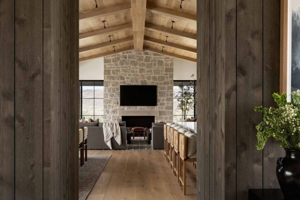 Hallway view through wood-paneled doorway framing great room stone fireplace and vaulted ceiling