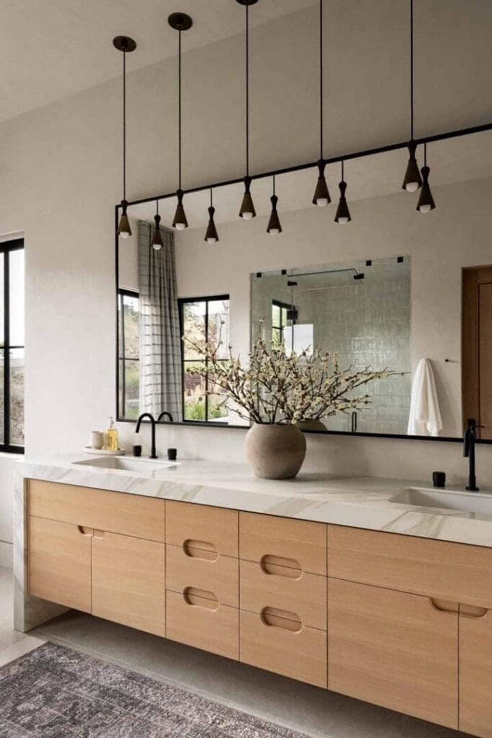 Primary bathroom double vanity with light oak cabinetry, marble countertop, and black-frame mirror