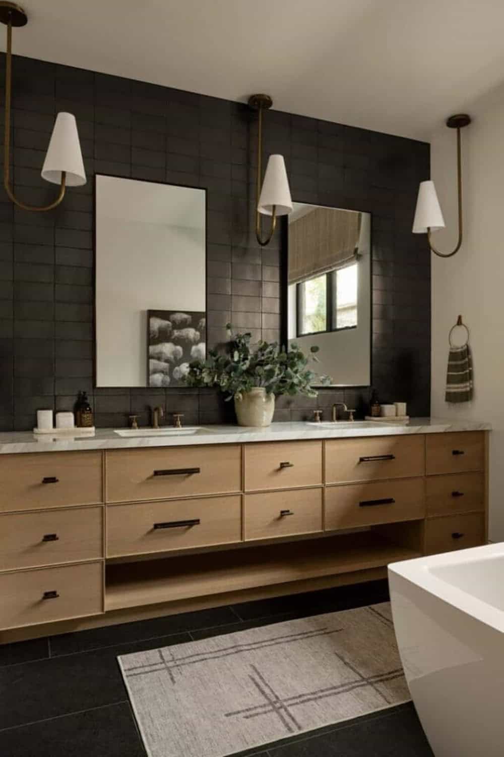 Guest bathroom with dark zellige tile wall, light oak floating vanity, and brass sconces
