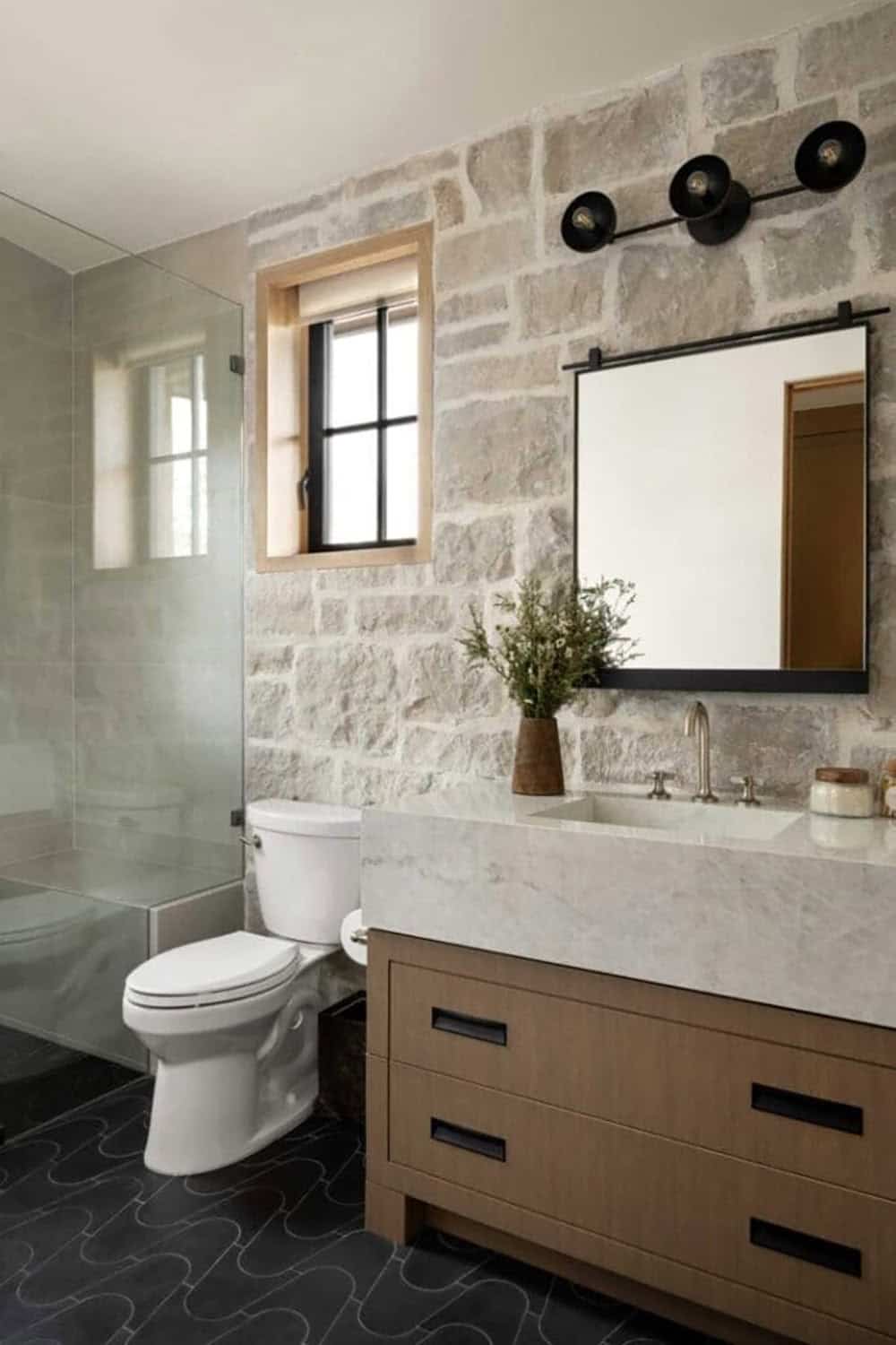 Guest bathroom with natural stone accent wall, wood vanity, marble countertop, and glass shower