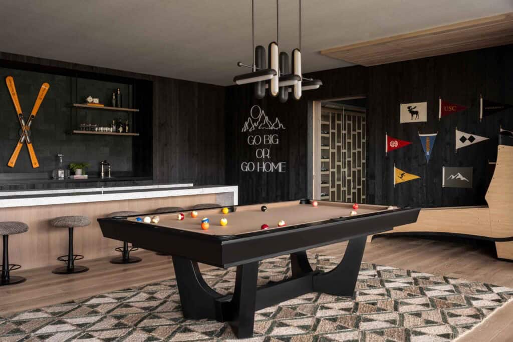 Dark game room with pool table, neon mountain sign, ski wall art, and college pennant flags