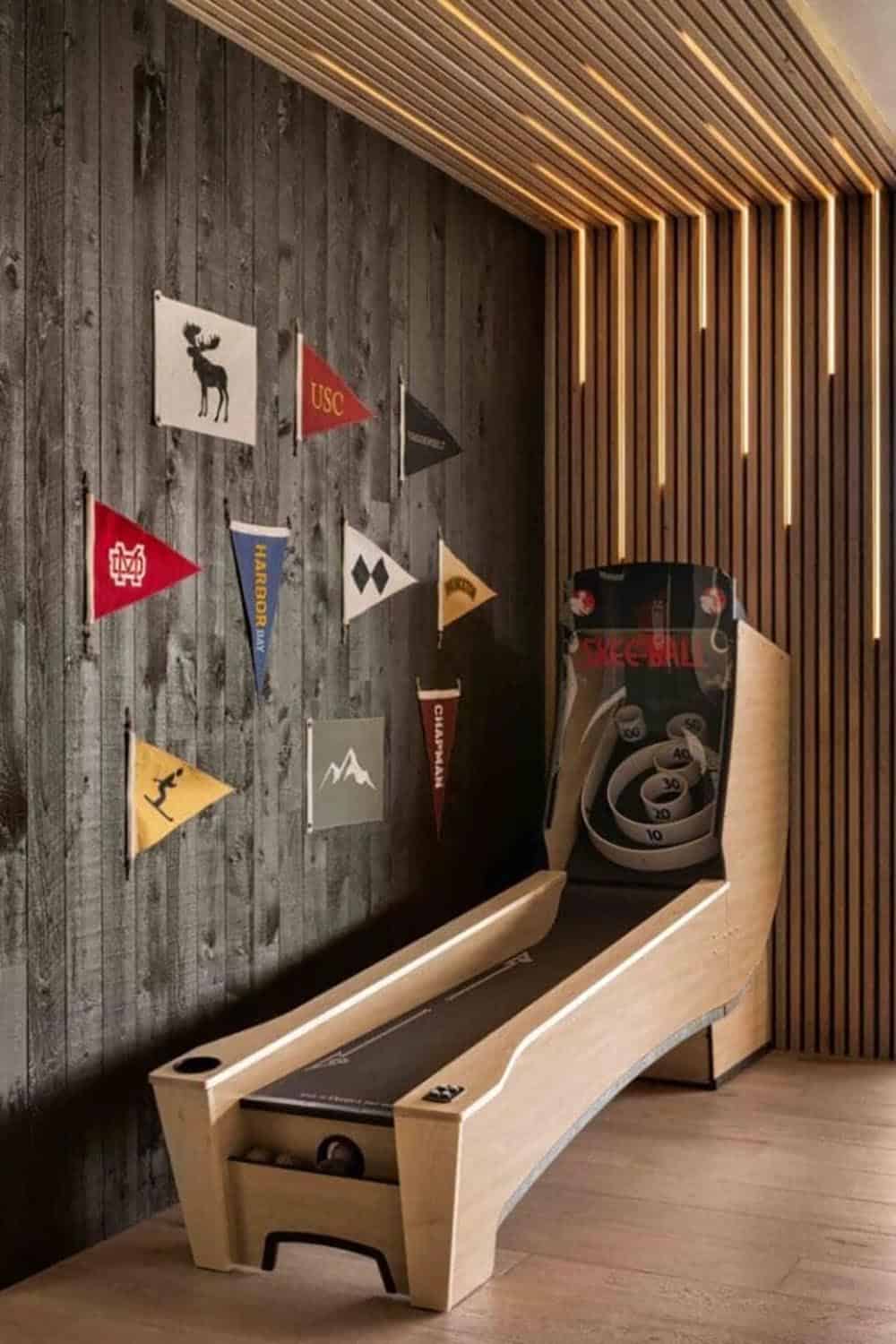 Skee-ball machine beside pennant flag wall with illuminated wood slat ceiling detail