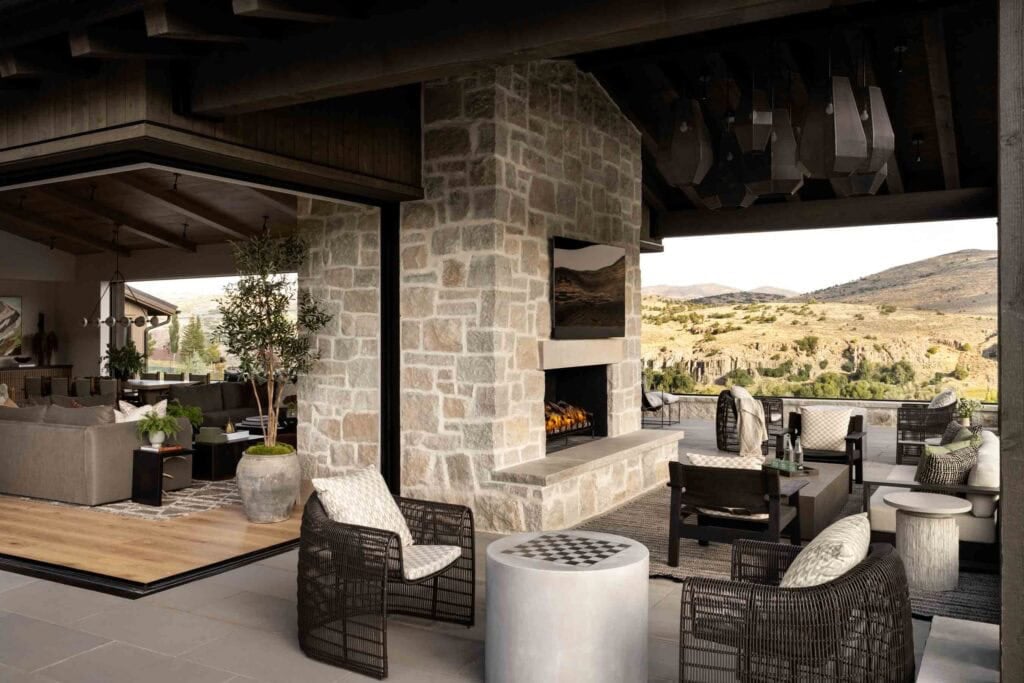 Covered outdoor patio with stone fireplace, wicker lounge chairs, and canyon views