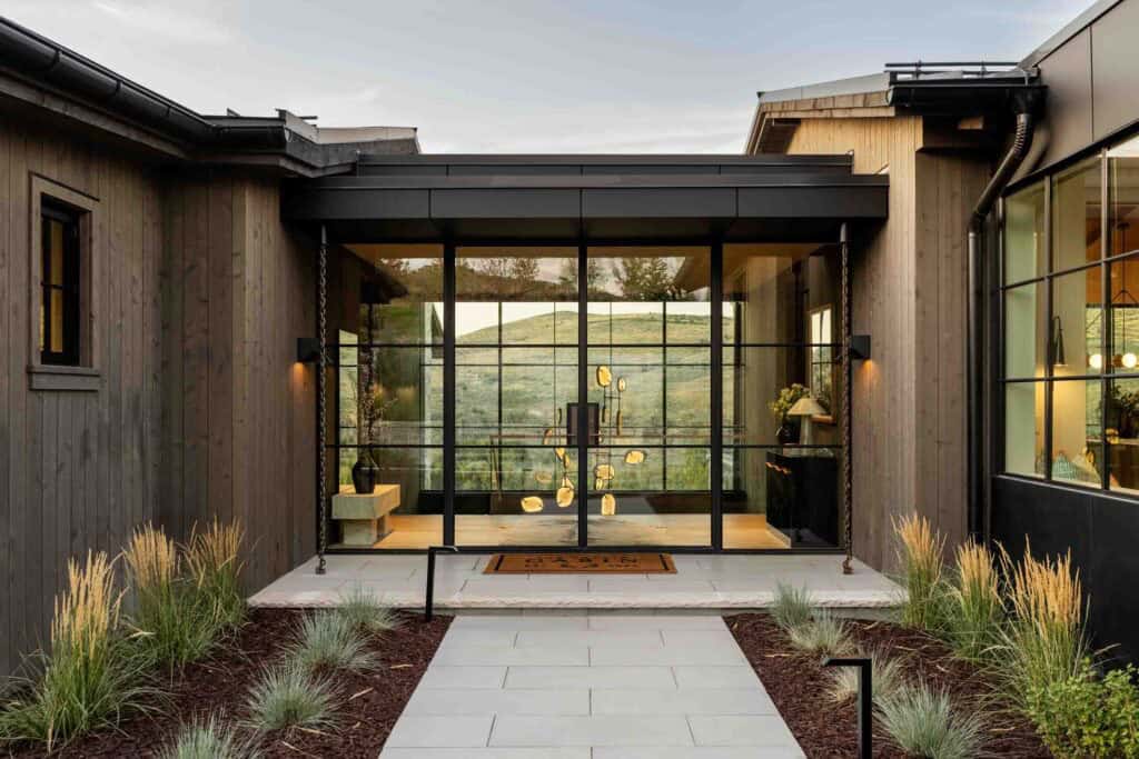 Glass-walled front entry with steel-frame curtain wall, sculptural pendant, and mountain views beyond
