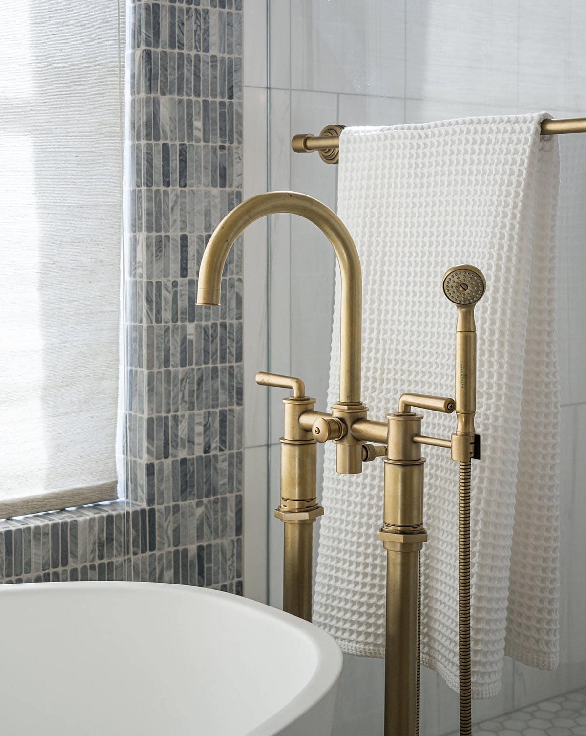 Antique brass freestanding tub filler with gray mosaic tile
