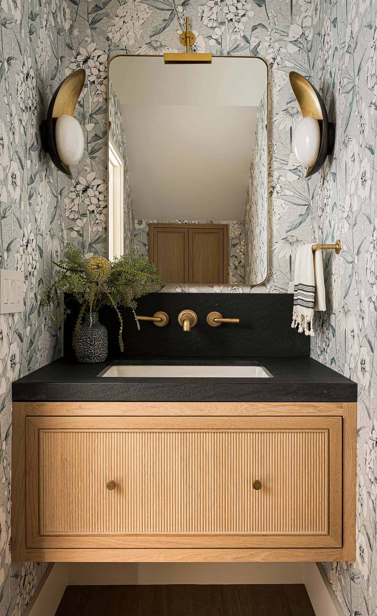 Powder room with floral wallpaper fluted vanity and brass fixtures