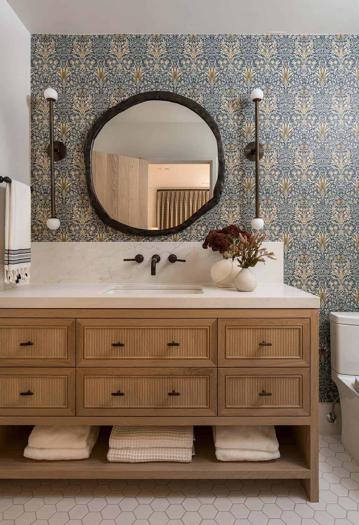 Guest bathroom with blue floral wallpaper, fluted oak vanity and round mirror