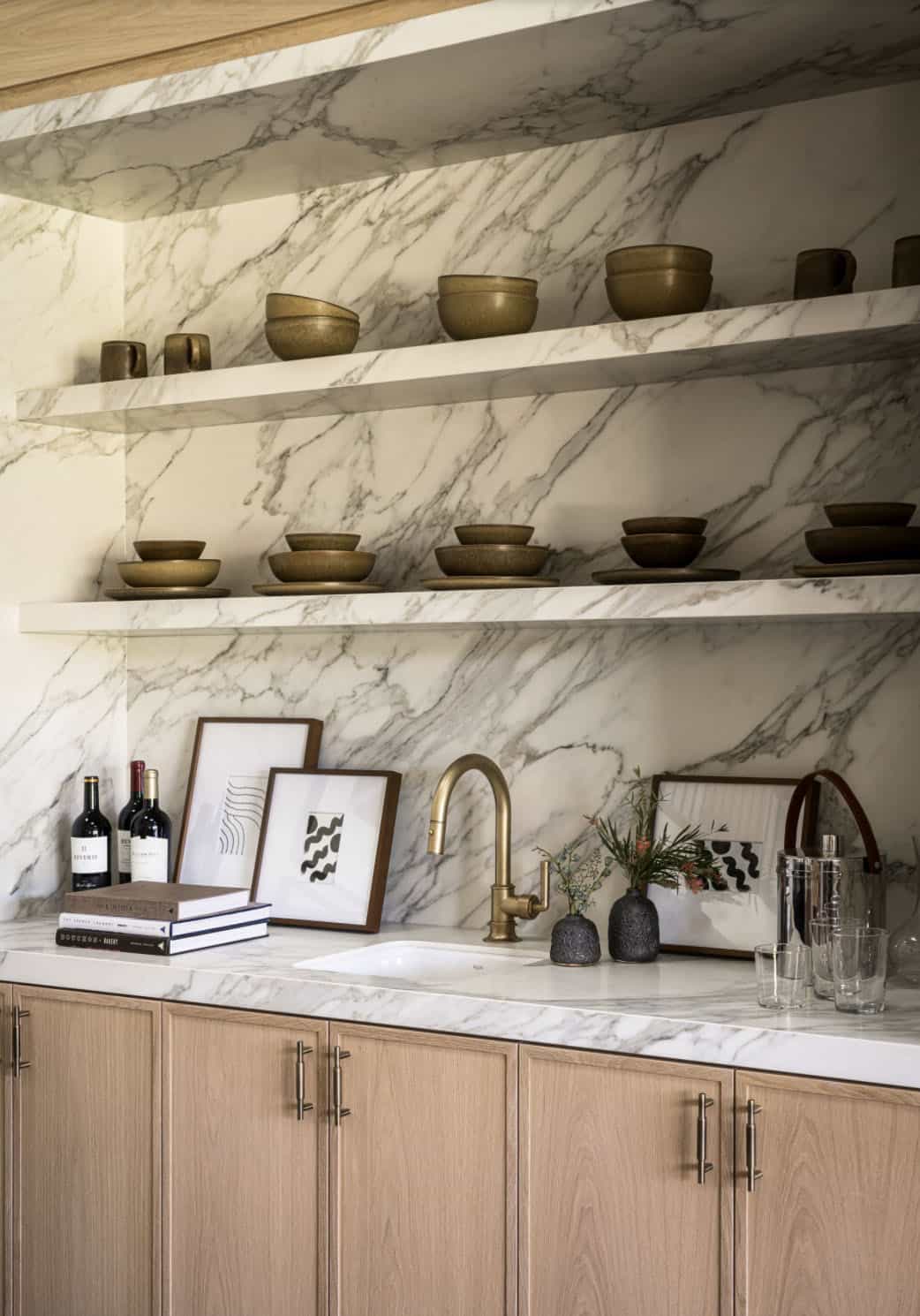Wet bar with marble backsplash open shelving and brass faucet